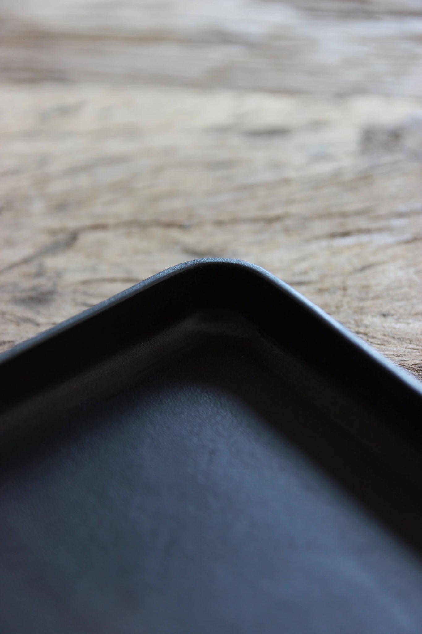Nahaufnahme der Kante einer Ablageschale aus Leder in Schwarz auf einer Holzplatte.