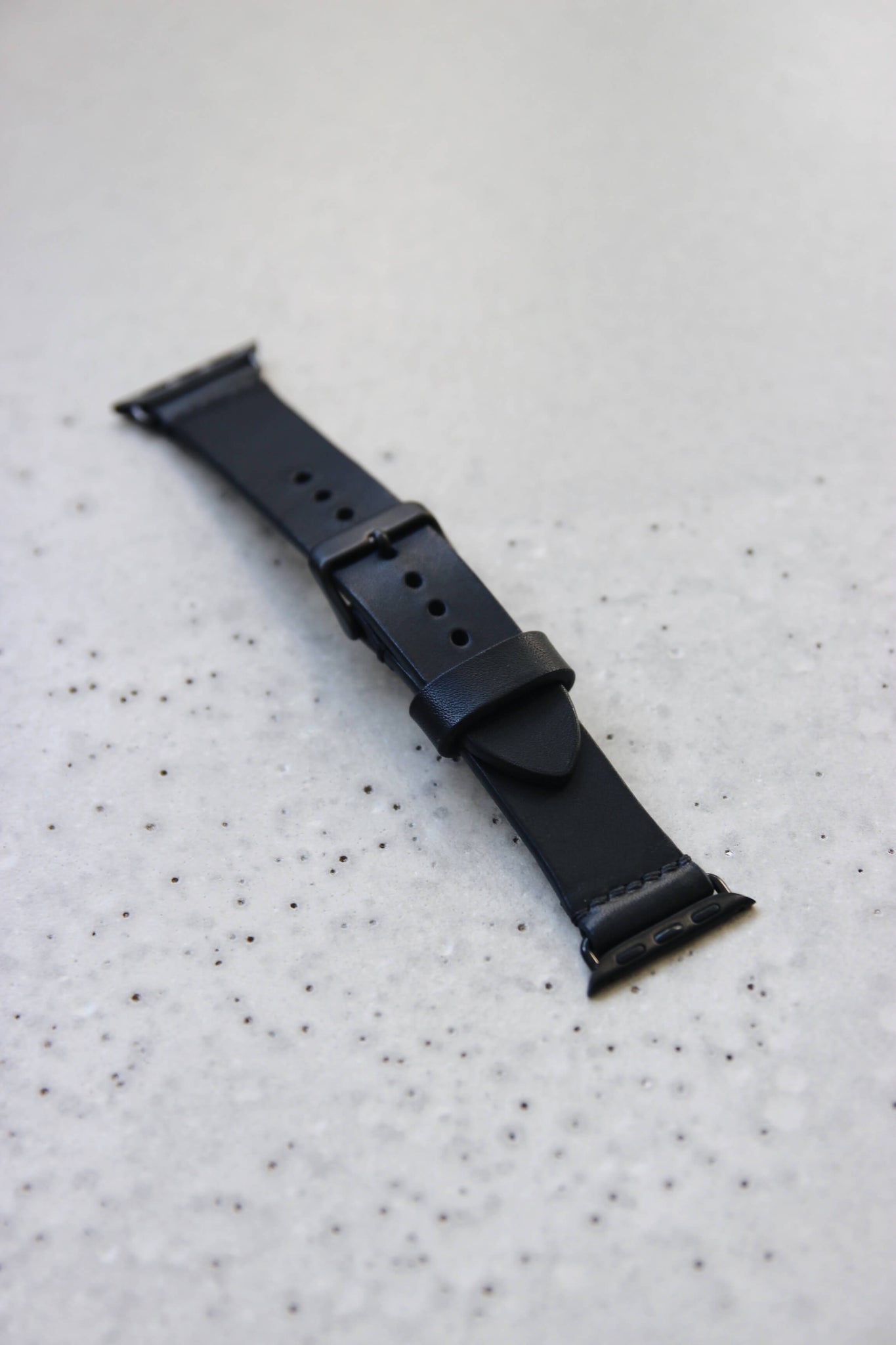 Apple Watch Lederband in Schwarz auf einem Betonboden liegend.