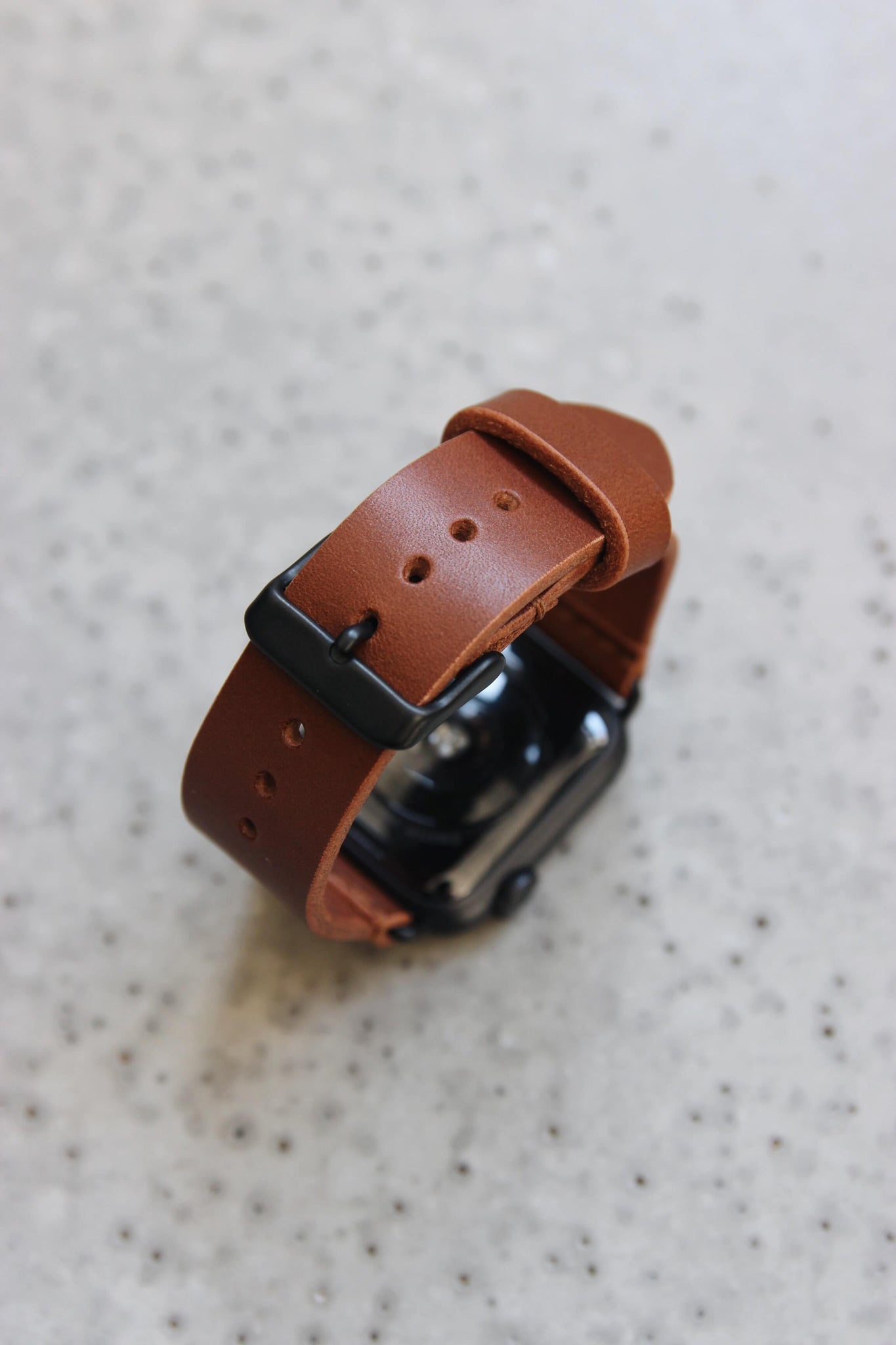 Eine Apple Watch mit einem Lederband in Braun auf einem Betonboden stehend.