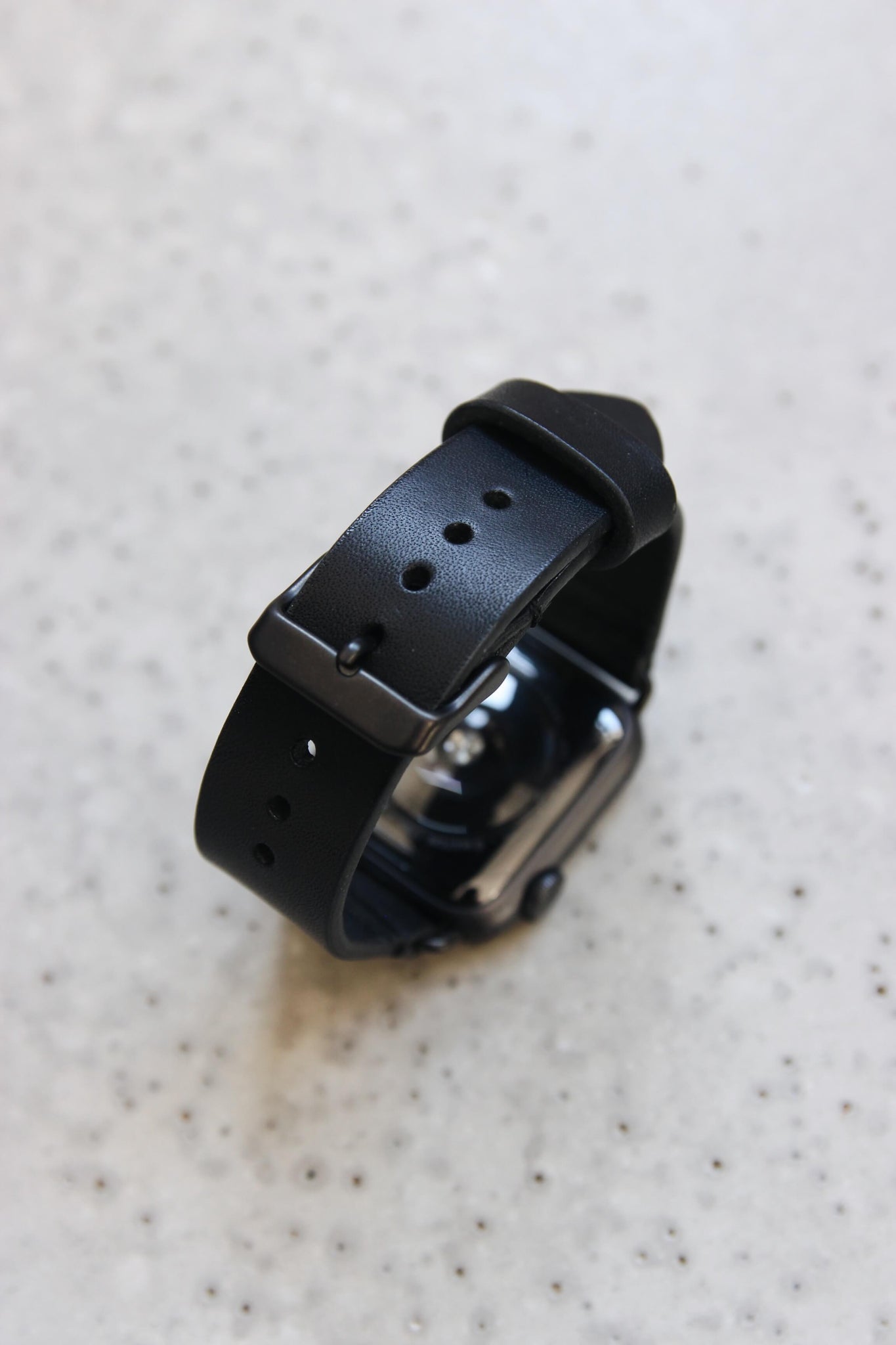 Eine Apple Watch mit einem Lederband in Schwarz auf einem Betonboden stehend.