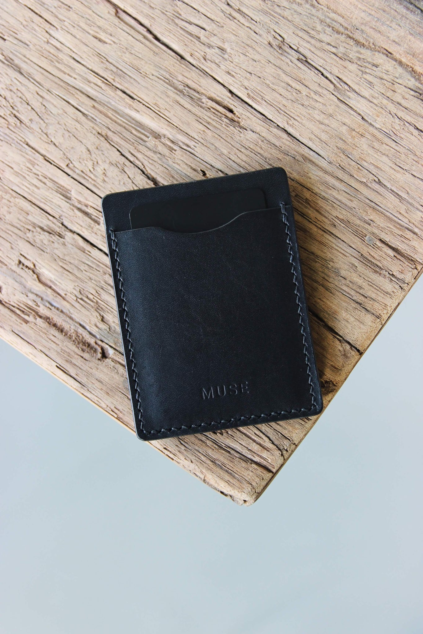 Auf einer Holzplatte liegt ein Kreditkartenetui aus Leder in Schwarz.