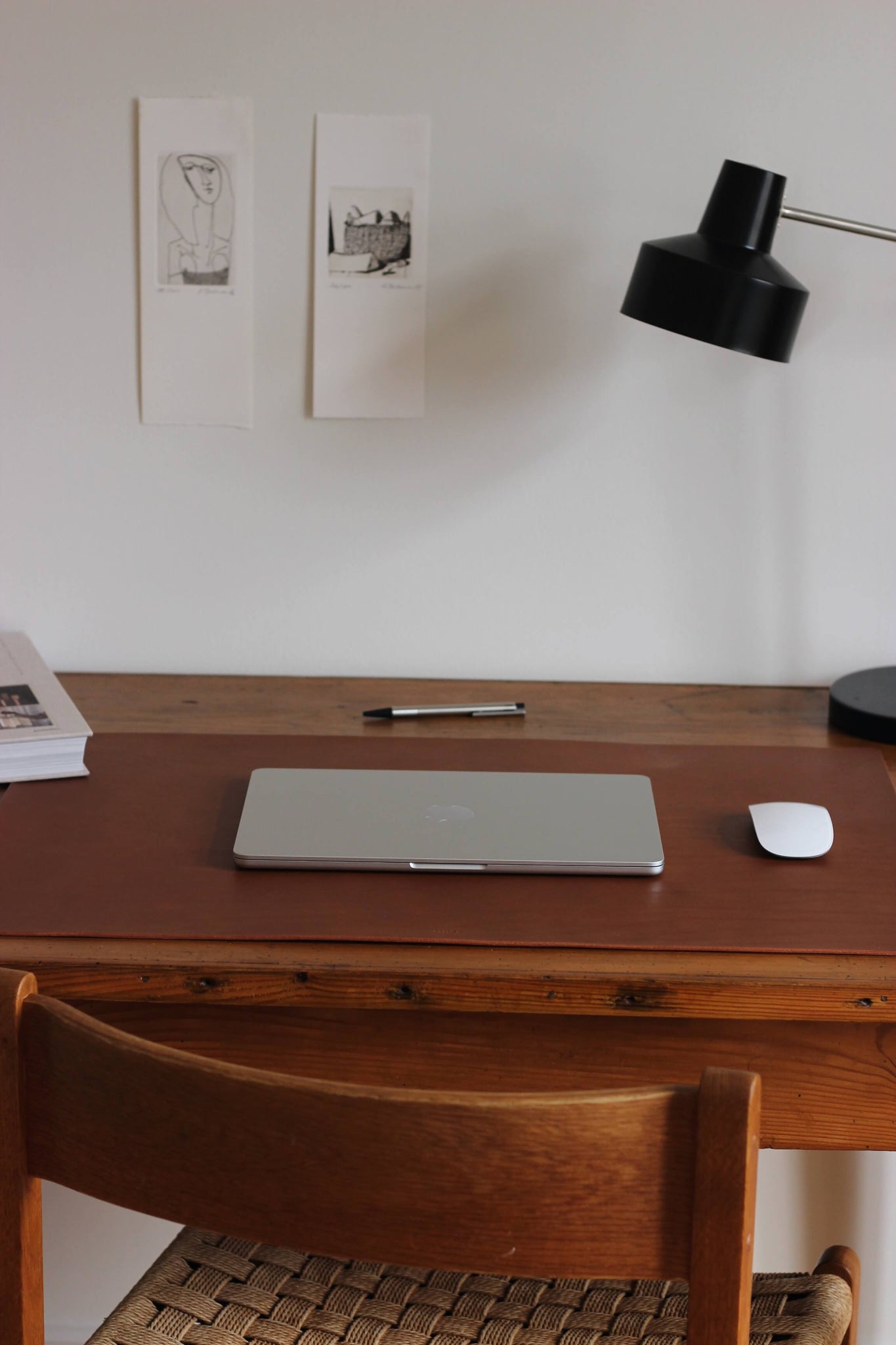 Eine Leder Schreibtischunterlage in Braun liegt auf einem Schreibtisch aus Holz und darauf befindet sich ein zugeklapptes MacBook und eine Maus.