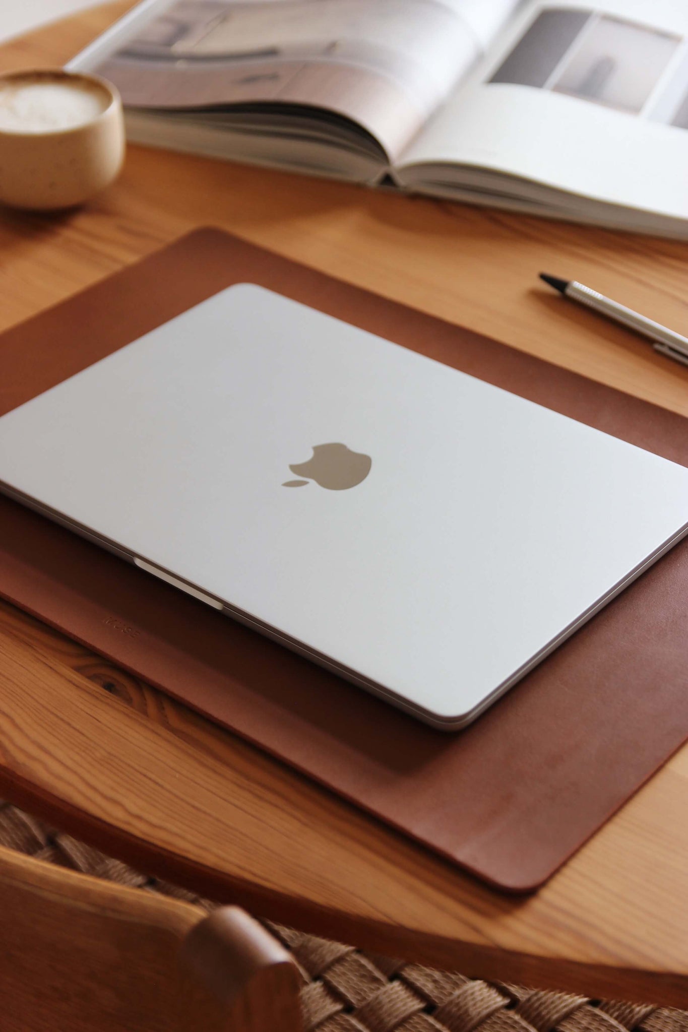 Seitenansicht einer Schreibtischunterlage aus Leder in Braun auf einem Holztisch und auf dieser befindet sich ein zugeklapptes MacBook.