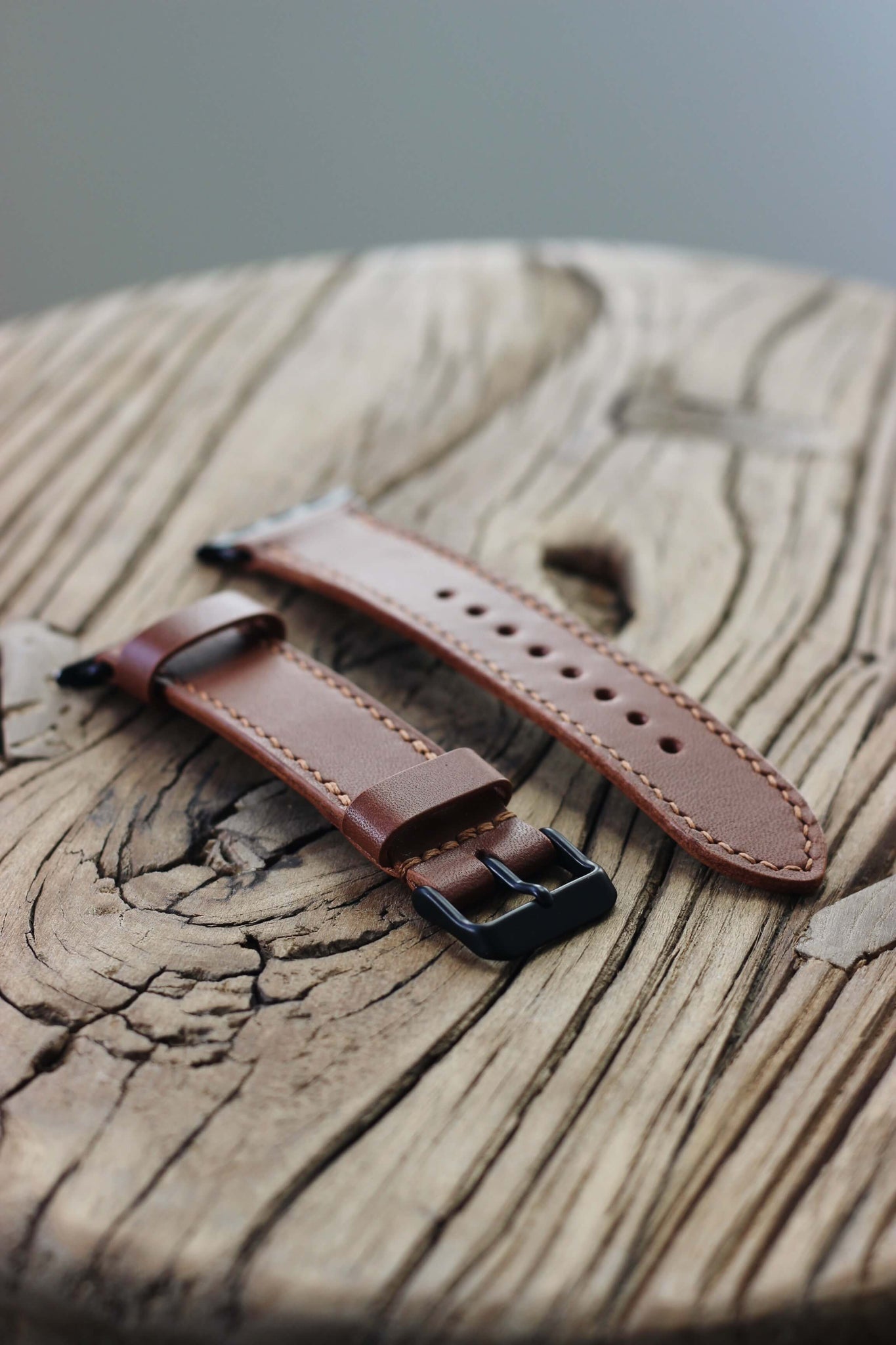 Seitenaufnahme eines Apple Watch Lederarmbands in Braun auf einem Holzhocker.