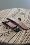 Seitenaufnahme eines Apple Watch Lederarmbands in Braun auf einem Holzhocker.