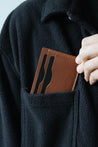 Kartenetui aus Leder in Braun wird in eine Brusttasche eines schwarzen Oberteils gesteckt.