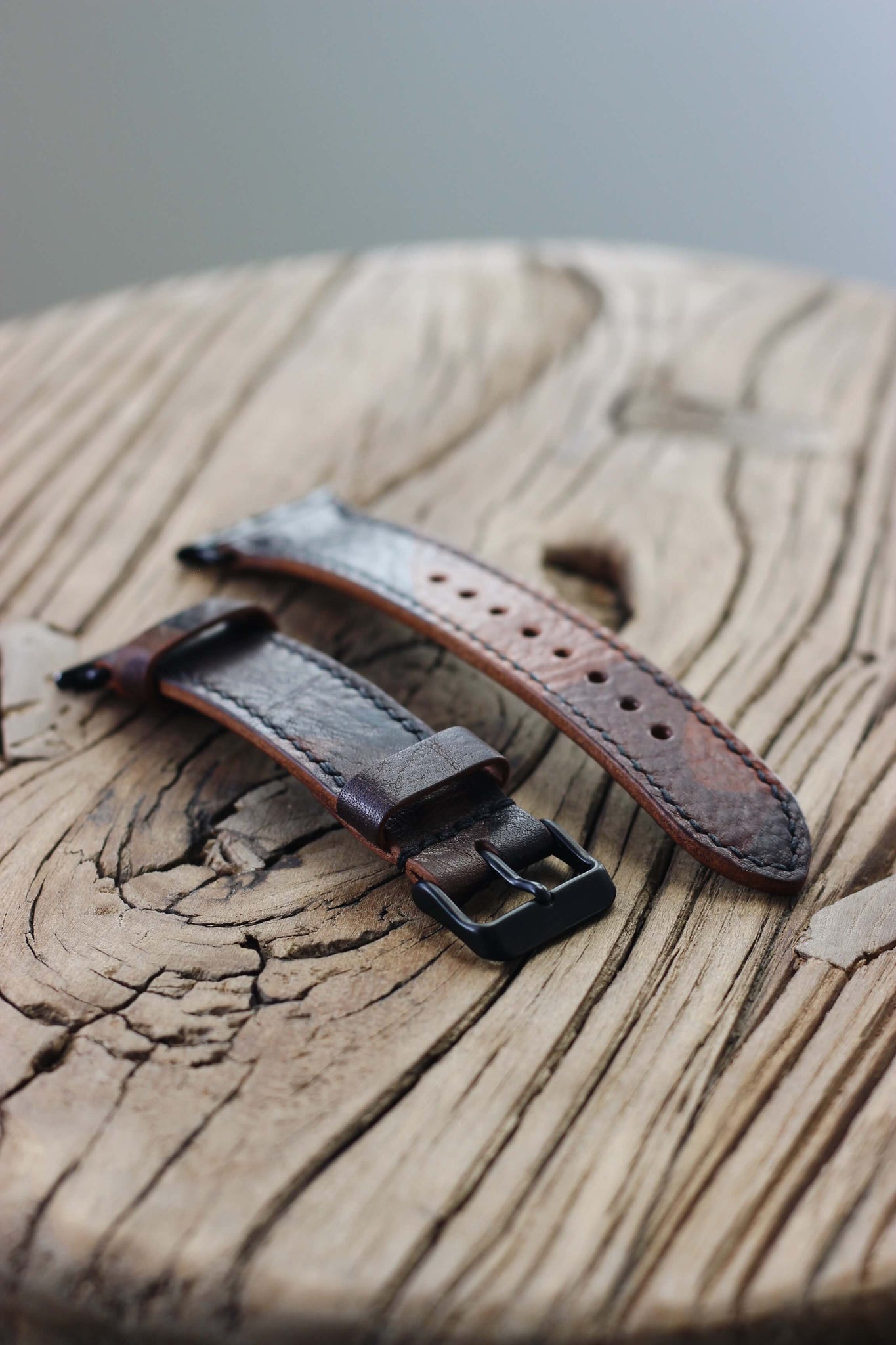 Seitenaufnahme eines Apple Watch Lederarmbands in Camo auf einem Holzhocker.