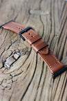 Apple Watch Lederarmband in Braun in der Seitenansicht auf einem Holzhocker.
