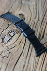 Apple Watch Lederarmband in Schwarz in der Seitenansicht auf einem Holzhocker.