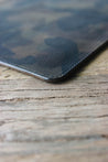 Nahaufnahme der Lederkante einer Leder MacBook Hülle in Camo auf einem Holztisch.