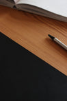 Ausschnitt einer Schreibtischunterlage aus Leder in Schwarz und ein Stift und ein aufgeklapptes Buch.
