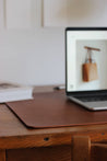 Ein aufgeklapptes MacBook steht auf einer Leder Schreibtischunterlage in Braun.