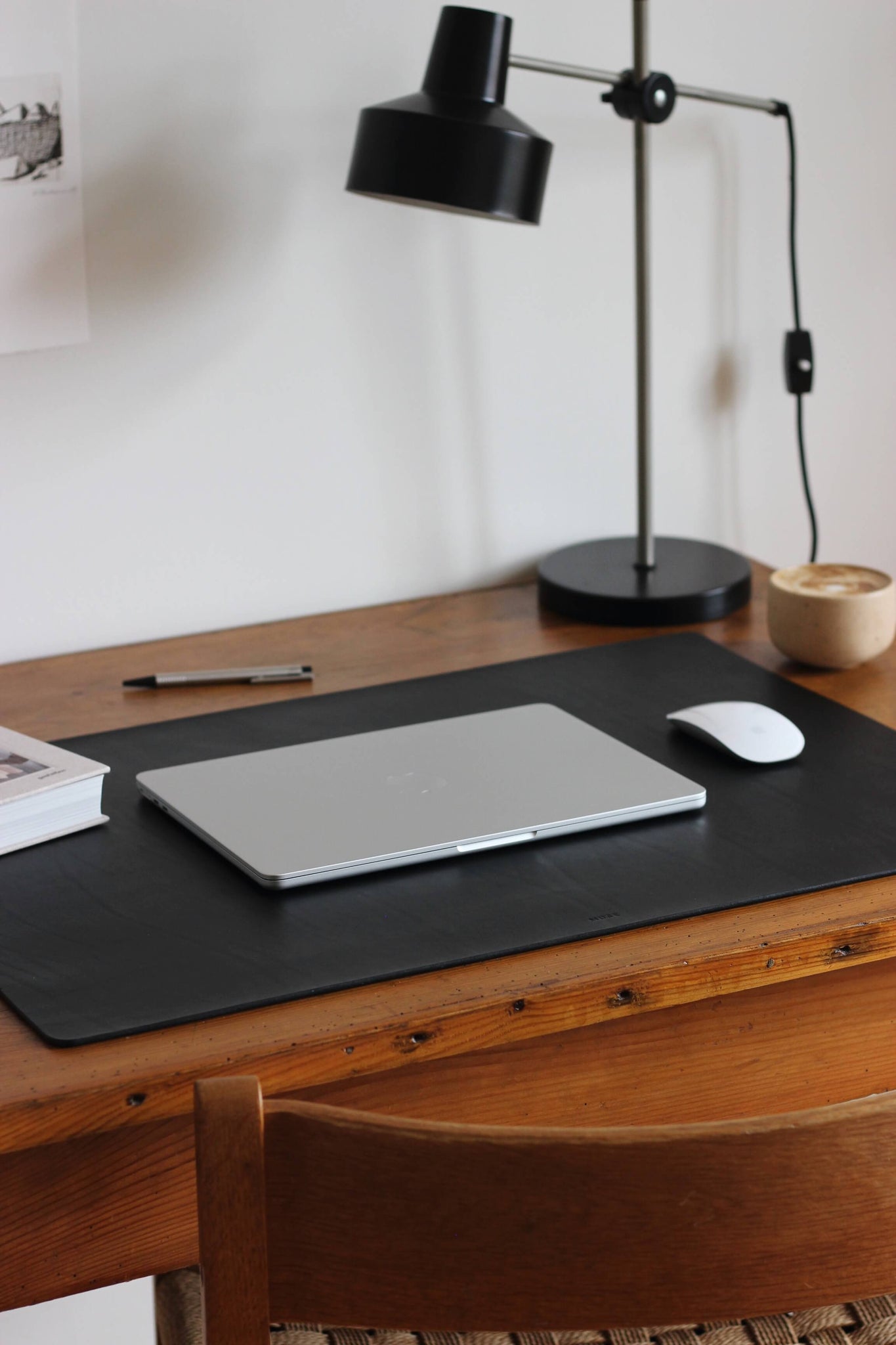 Seitliche Ansicht einer Leder Schreibtischunterlage in Schwarz auf einem Holzschreibtisch und darauf liegt ein zugeklapptes MacBook und eine Maus.