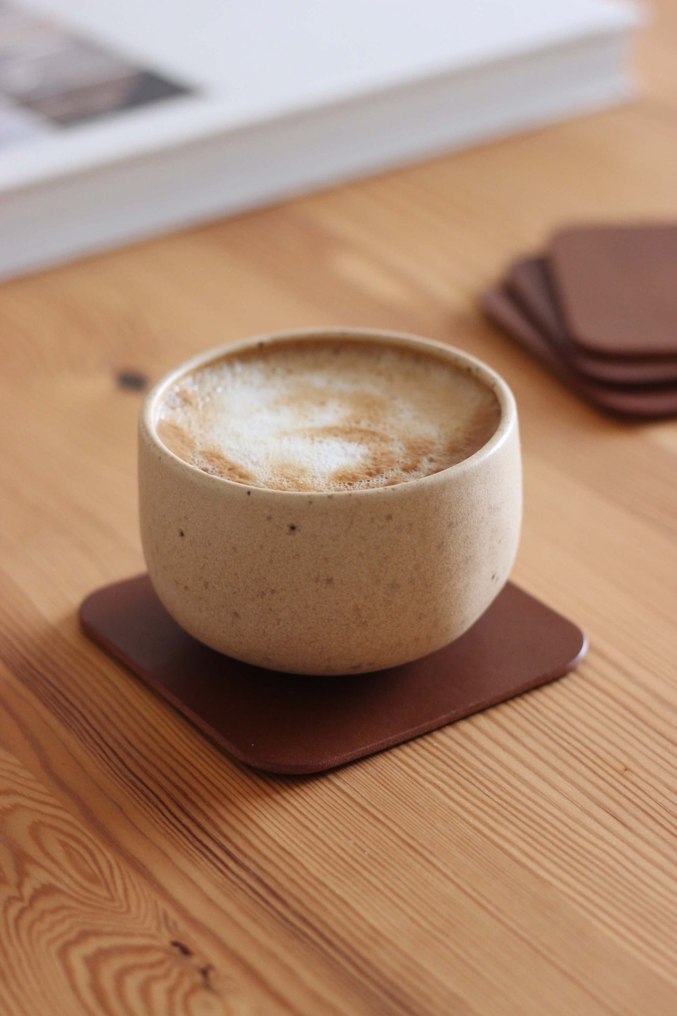 Eine Kaffeetasse steht auf einem Leder Untersetzer in Braun auf einem Holztisch.