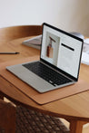 Ein aufgeklapptes MacBook liegt auf einer Schreibtischunterlage aus Leder in Natural auf einem Holztisch.