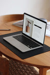 Ein aufgeklapptes MacBook liegt auf einer Schreibtischunterlage aus Leder in Schwarz auf einem Holztisch.