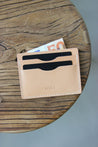 Auf einem Holzstuhl liegt ein Kartenetui aus Leder in Natural und aus diesem guckt oben ein 50€-Schein heraus.