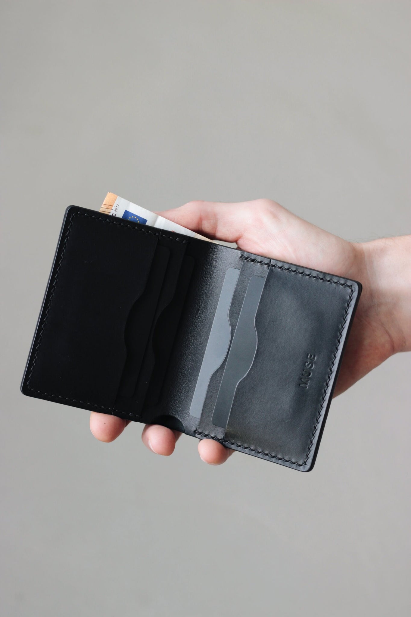 Eine Hand hält ein geöffnetes Leder Kartenetui in Schwarz.