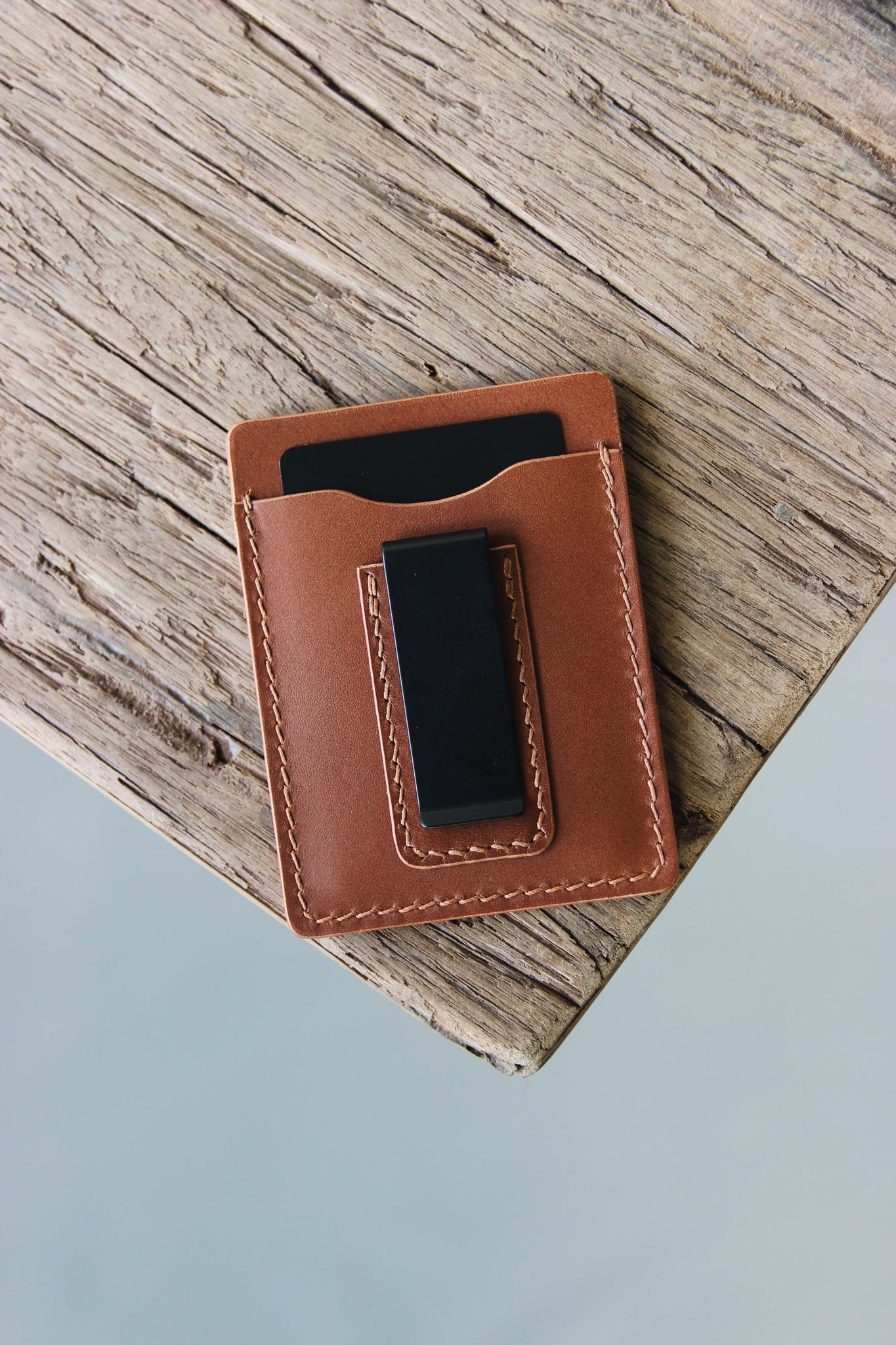 Ein Kreditkartenetui aus Leder in Braun mit integrierter Geldklammer liegt auf einer Holzplatte.