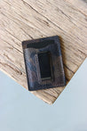 Ein Kreditkartenetui aus Leder in Camo mit integrierter Geldklammer liegt auf einer Holzplatte.
