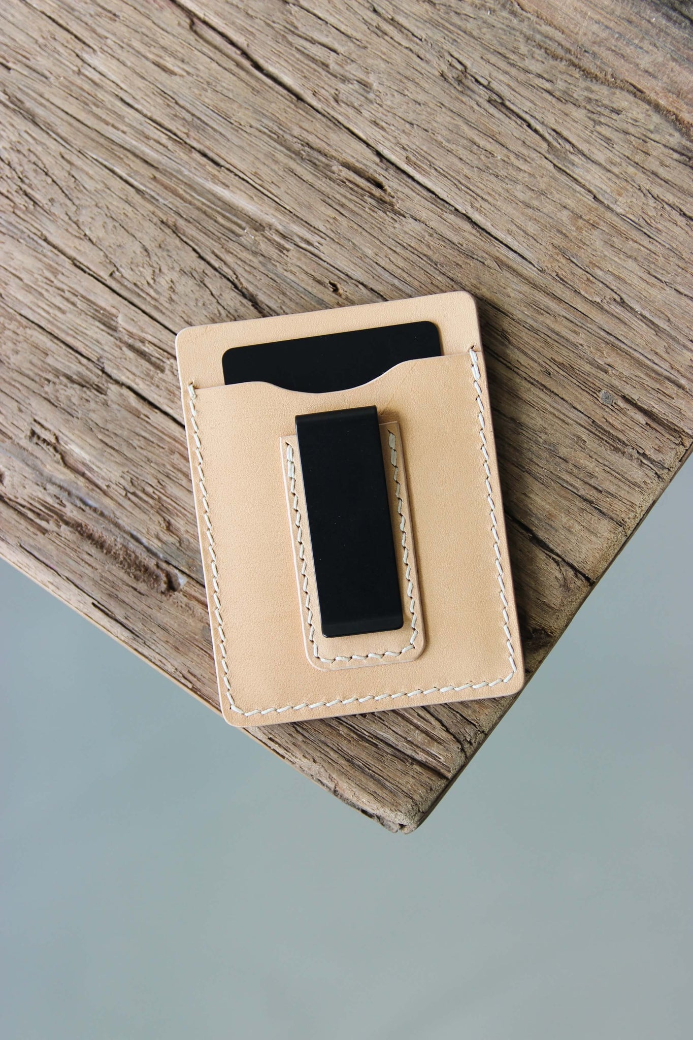 Ein Kreditkartenetui aus Leder in Natural mit integrierter Geldklammer liegt auf einer Holzplatte.