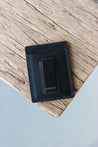 Ein Kreditkartenetui aus Leder in Schwarz mit integrierter Geldklammer liegt auf einer Holzplatte.