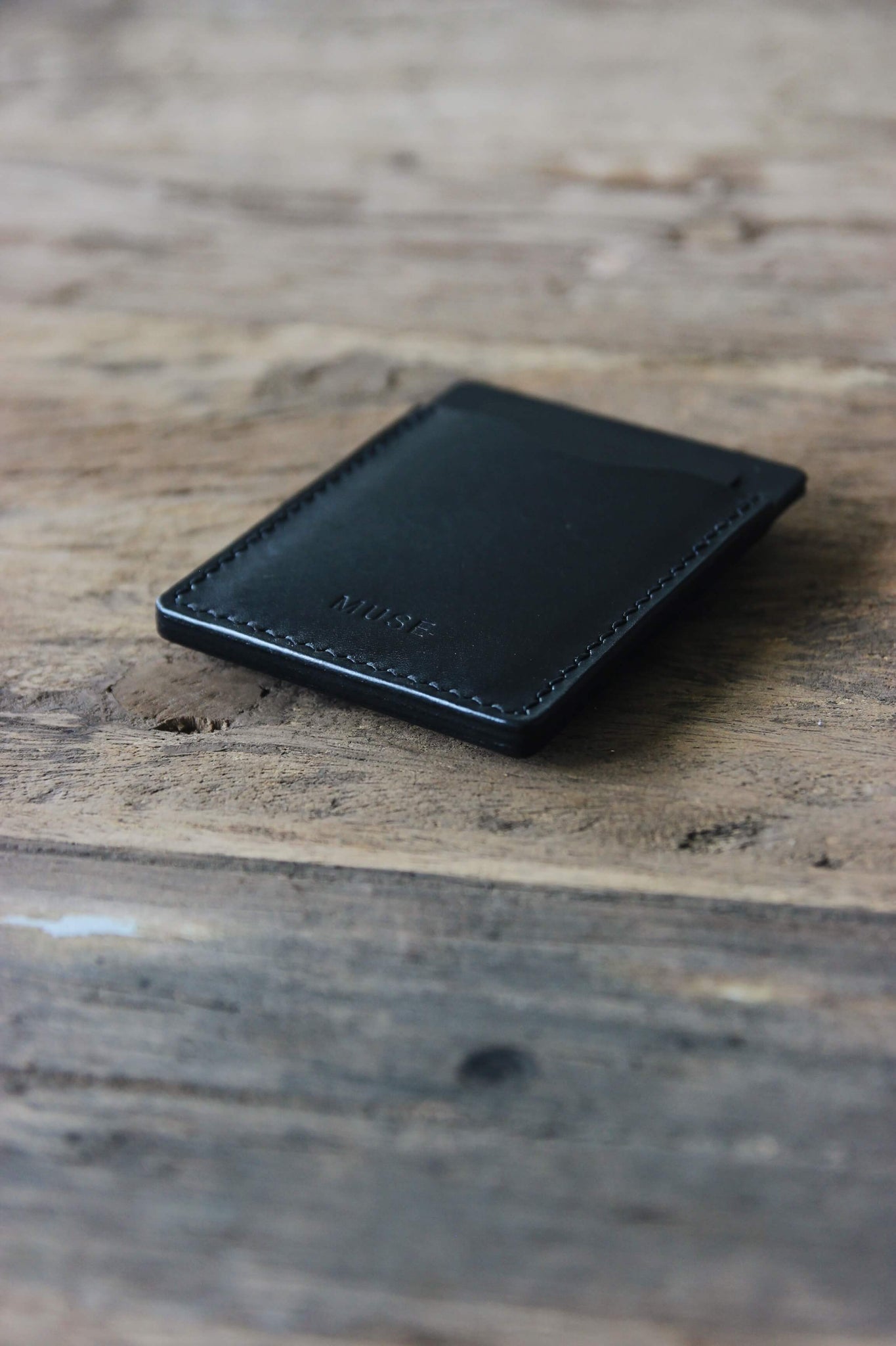 Seitliche Detailaufnahme eines Kreditkartenetuis aus Leder in Schwarz auf einer Holzplatte.