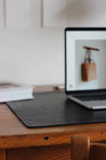 Ein aufgeklapptes MacBook steht auf einer Leder Schreibtischunterlage in Schwarz.
