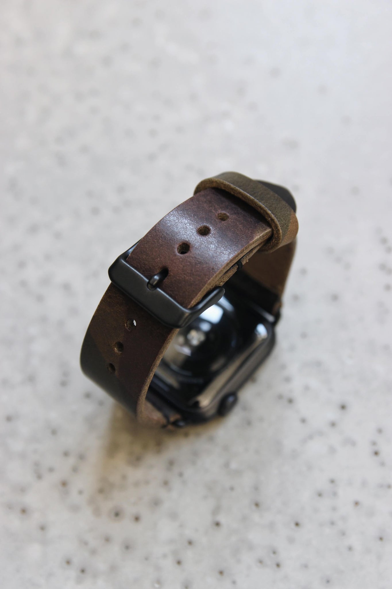 Eine Apple Watch mit einem Lederband in Camouflage auf einem Betonboden stehend.