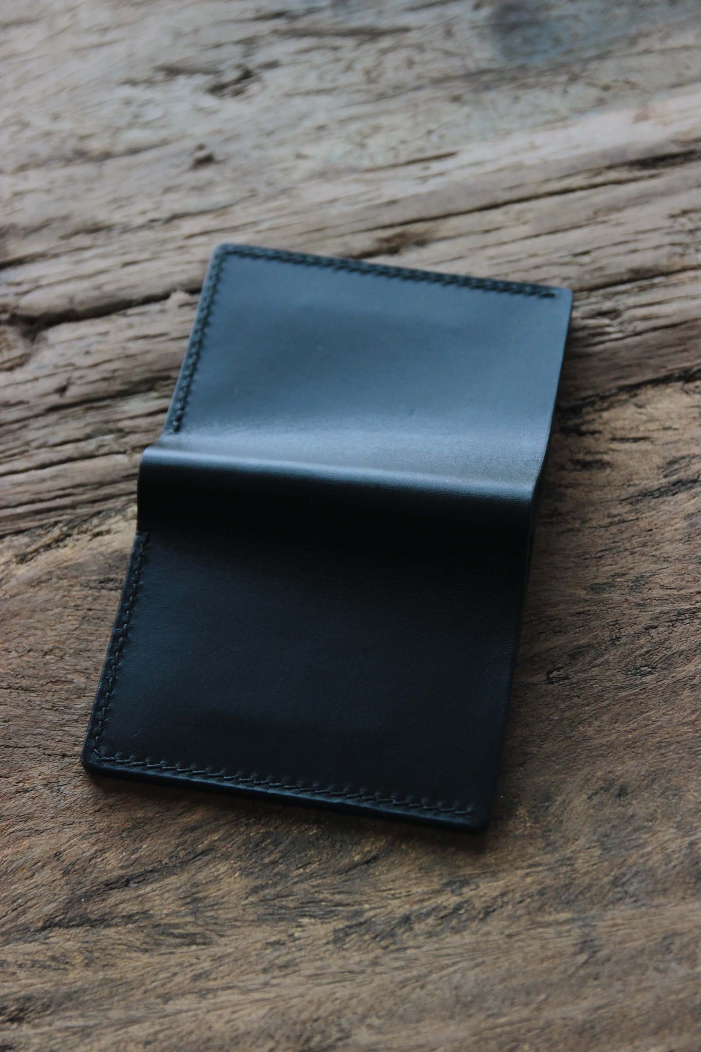 Rückseite eines Leder Kartenetuis in Schwarz auf einer Holzplatte.