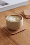 Eine Kaffeetasse steht auf einem Leder Untersetzer in Natur auf einem Holztisch.