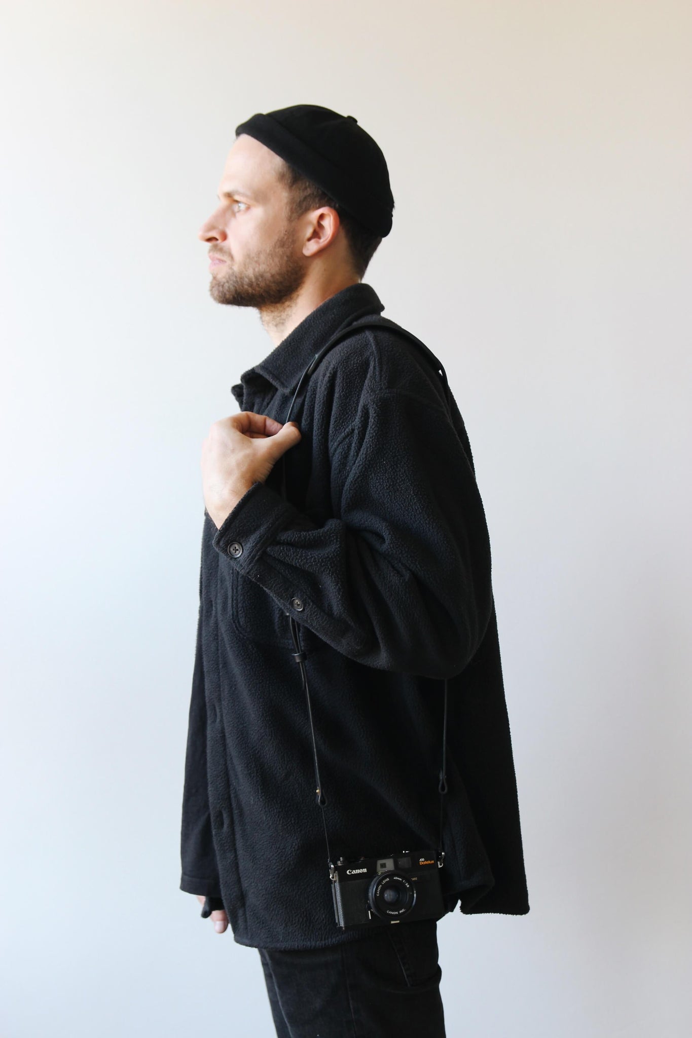 Seitliche Aufnahme von einem schwarz gekleideten Mann mit einem Leder Kameragurt in Schwarz über der Schulter.