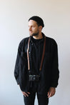 Ein Mann mit schwarzer Kleidung trägt eine Kamera mit einem Leder Kameragurt in Braun um den Hals.
