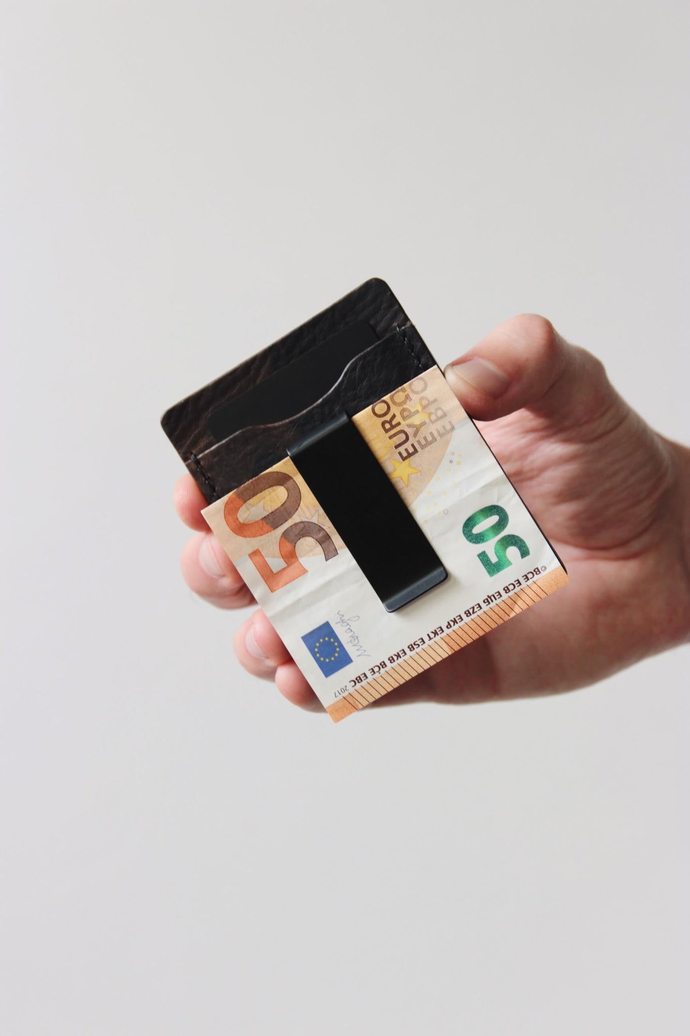 Eine Hand hält ein Kreditkartenetui aus Leder in Camo und in der integrierten Geldklammer steckt ein 50€-Schein.