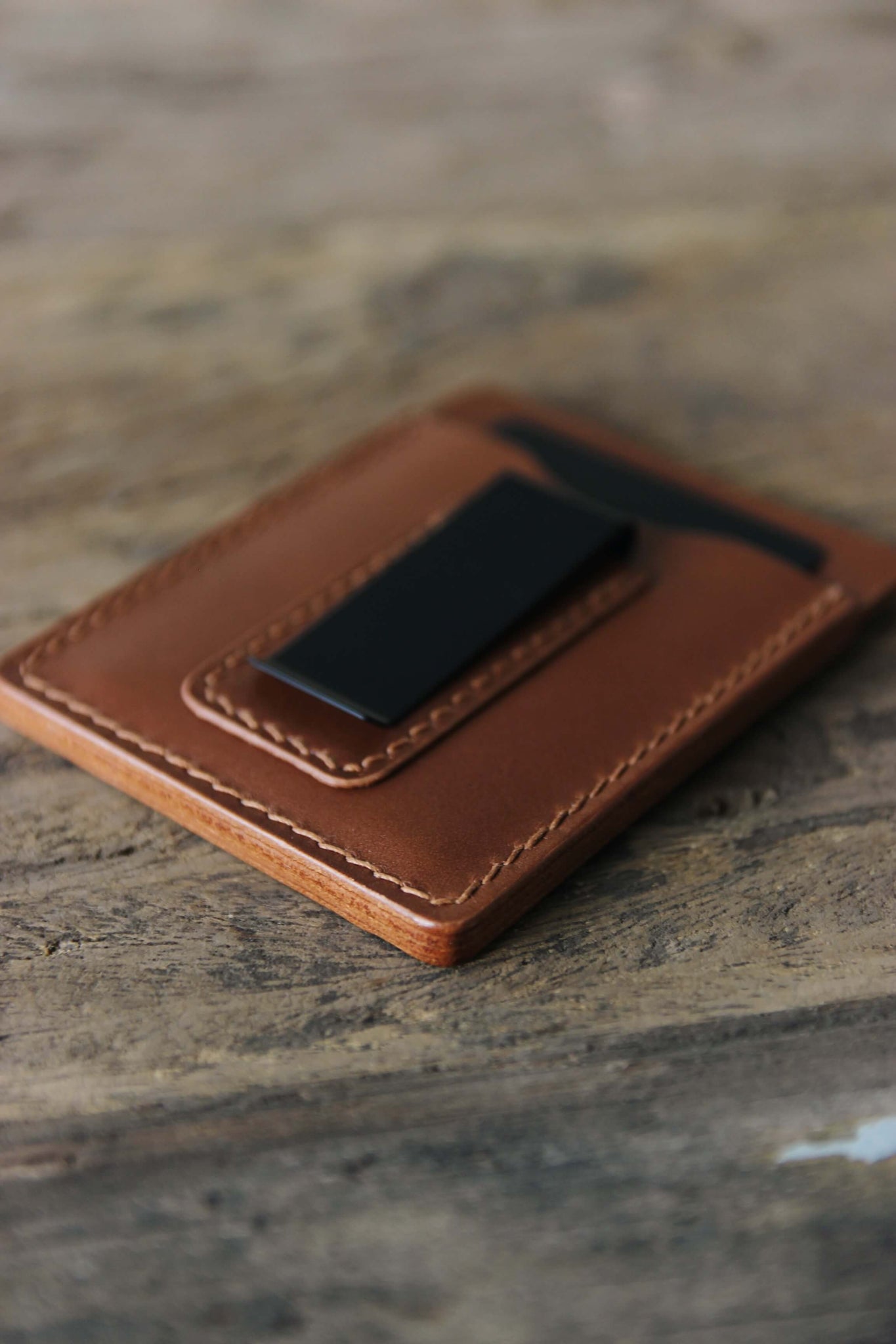 Nahaufnahme der schwarzen Geldklammer eines Kreditkartenetuis aus Leder in Braun auf einer Holzplatte liegend.