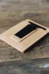 Nahaufnahme der schwarzen Geldklammer eines Kreditkartenetuis aus Leder in Natural auf einer Holzplatte liegend.