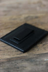 Nahaufnahme der schwarzen Geldklammer eines Kreditkartenetuis aus Leder in Schwarz auf einer Holzplatte liegend.
