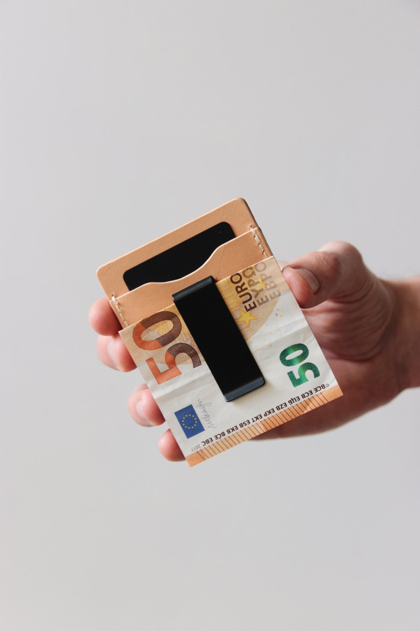 Eine Hand hält ein Kreditkartenetui aus Leder in Natural und in der integrierten Geldklammer steckt ein 50€-Schein.