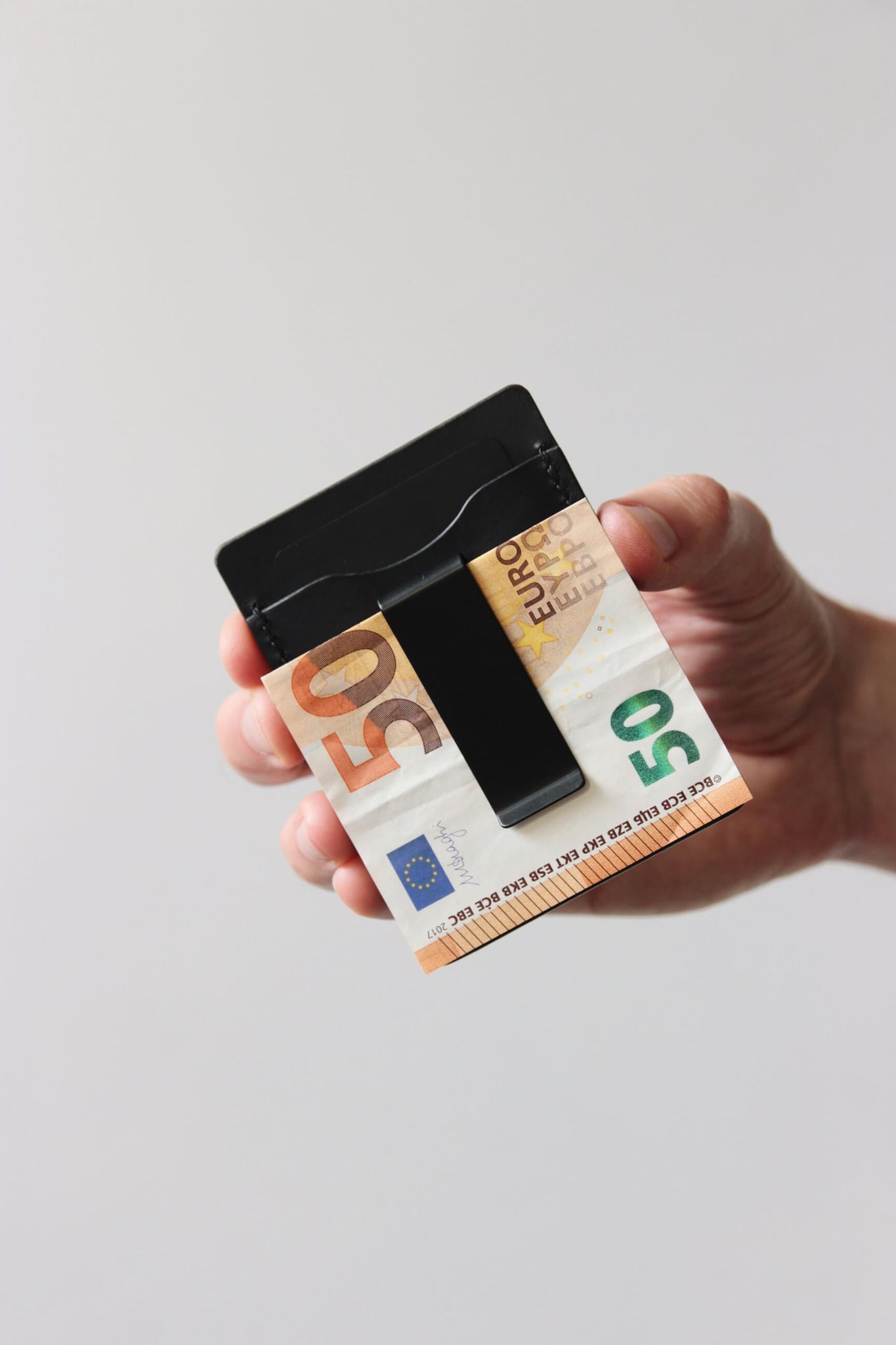 Eine Hand hält ein Kreditkartenetui aus Leder in Schwarz und in der integrierten Geldklammer steckt ein 50€-Schein.