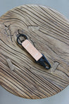 Ein Leder Schlüsselanhänger in Natural mit einem Karabiner und Schlüsselring in Schwarz auf einem Holzstuhl.
