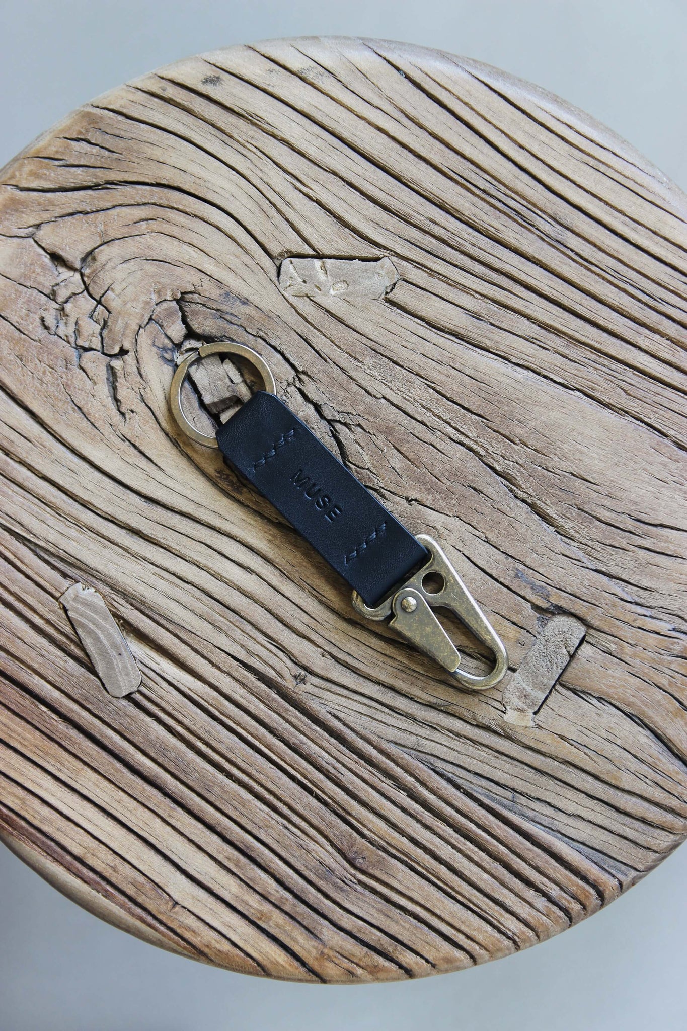 Ein Leder Schlüsselanhänger in Schwarz mit einem Karabiner und Schlüsselring in Messing Antik auf einem Holzstuhl.