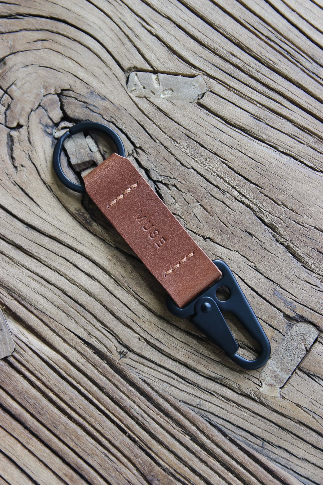 Nahaufnahme eines Leder Schlüsselanhängers in Braun mit einem Karabiner und Schlüsselring in Schwarz auf einem Holzstuhl.