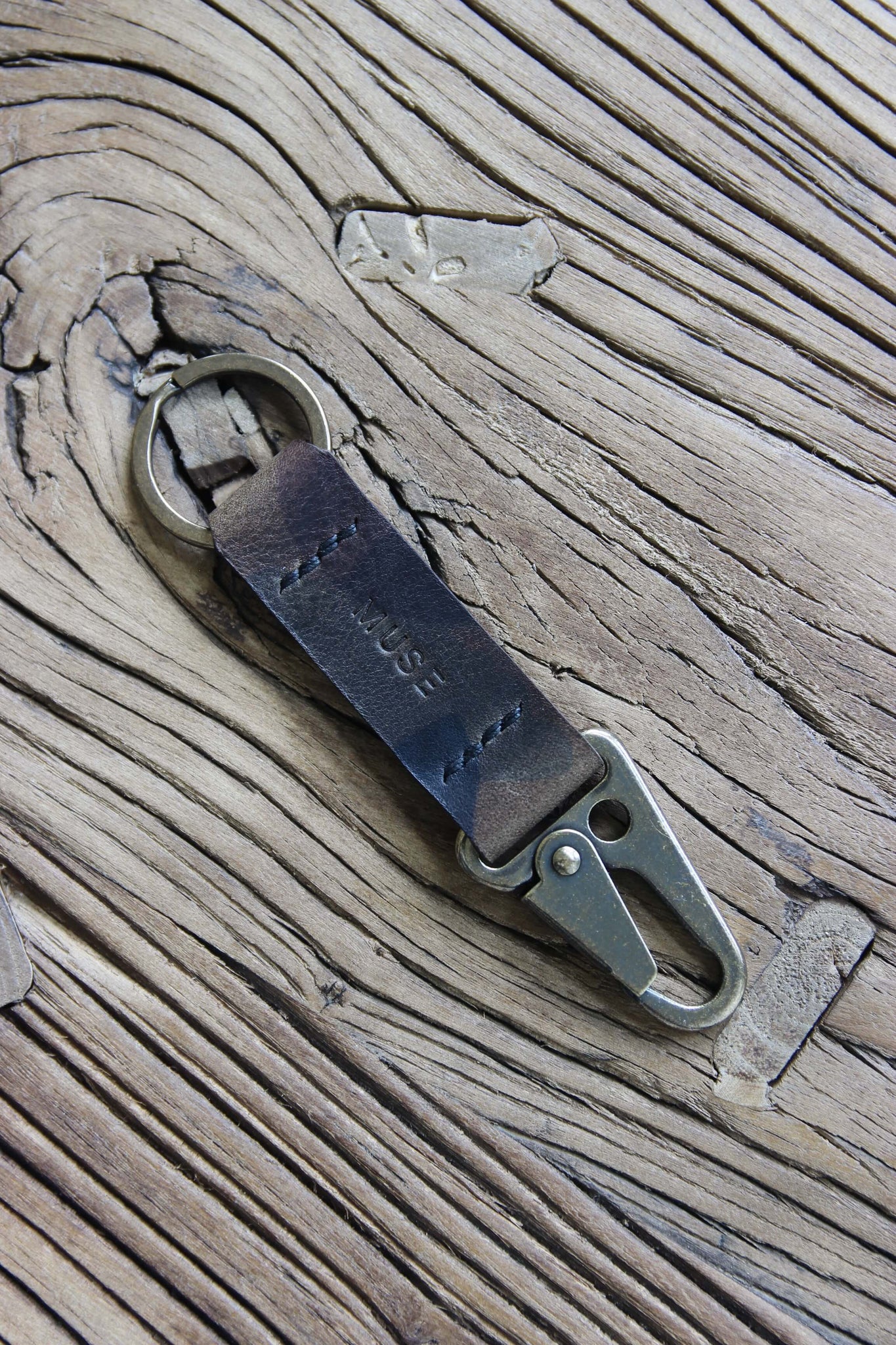 Nahaufnahme eines Leder Schlüsselanhängers in Camo mit einem Karabiner und Schlüsselring in Messing Antik auf einem Holzstuhl.
