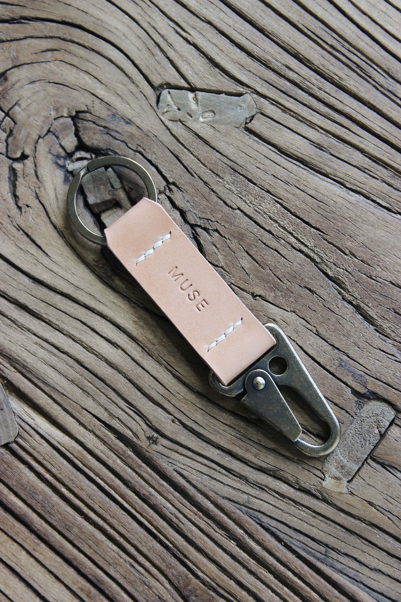 Nahaufnahme eines Leder Schlüsselanhängers in Natural mit einem Karabiner und Schlüsselring in Messing Antik auf einem Holzstuhl.
