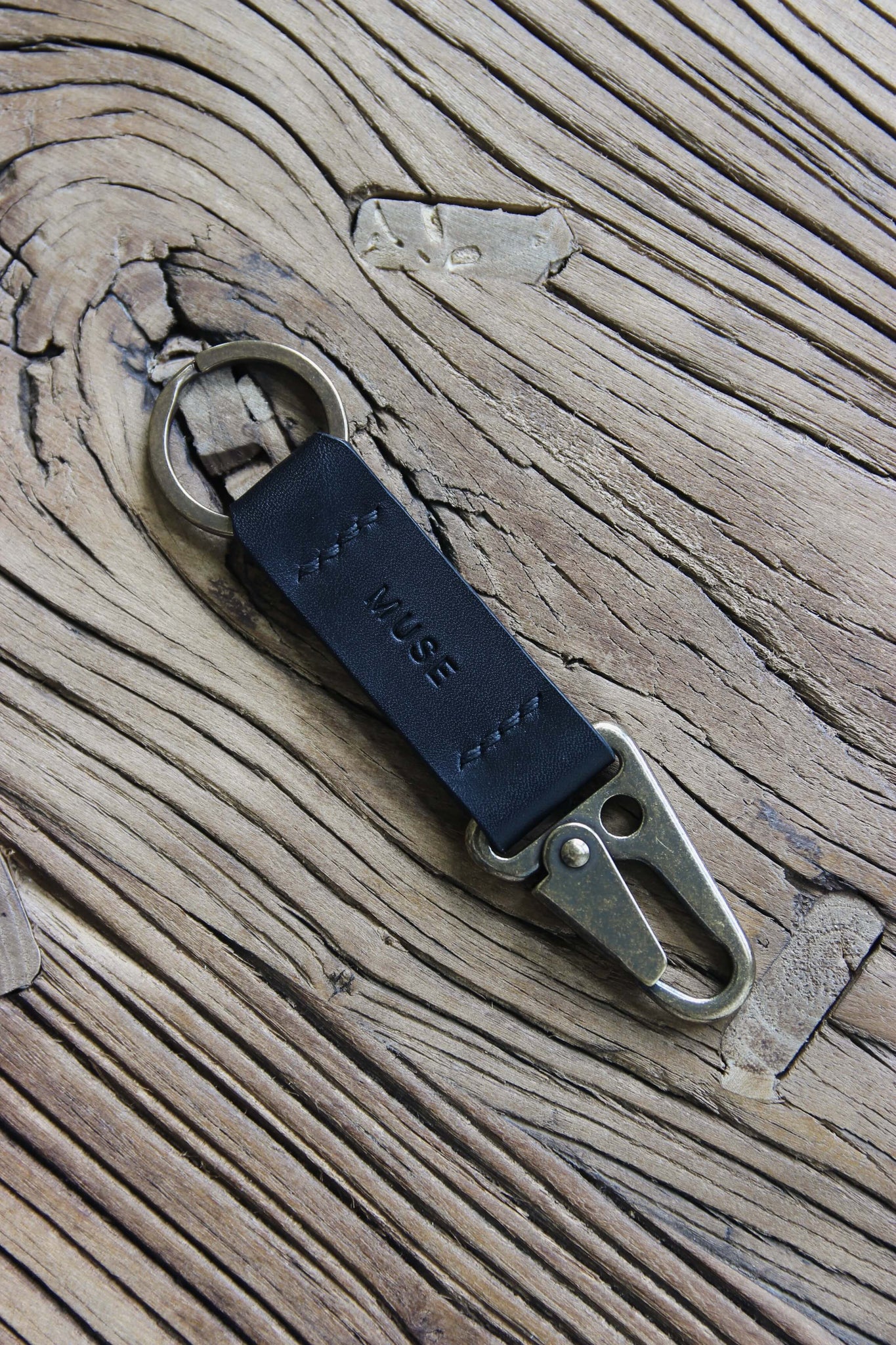 Nahaufnahme eines Leder Schlüsselanhängers in Schwarz mit einem Karabiner und Schlüsselring in Messing Antik auf einem Holzstuhl.