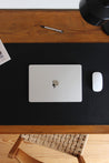 Nahaufnahme einer Leder Schreibtischunterlage in Schwarz auf einem Schreibtisch aus Holz und auf dieser liegt ein zugeklapptes MacBook und eine Maus.