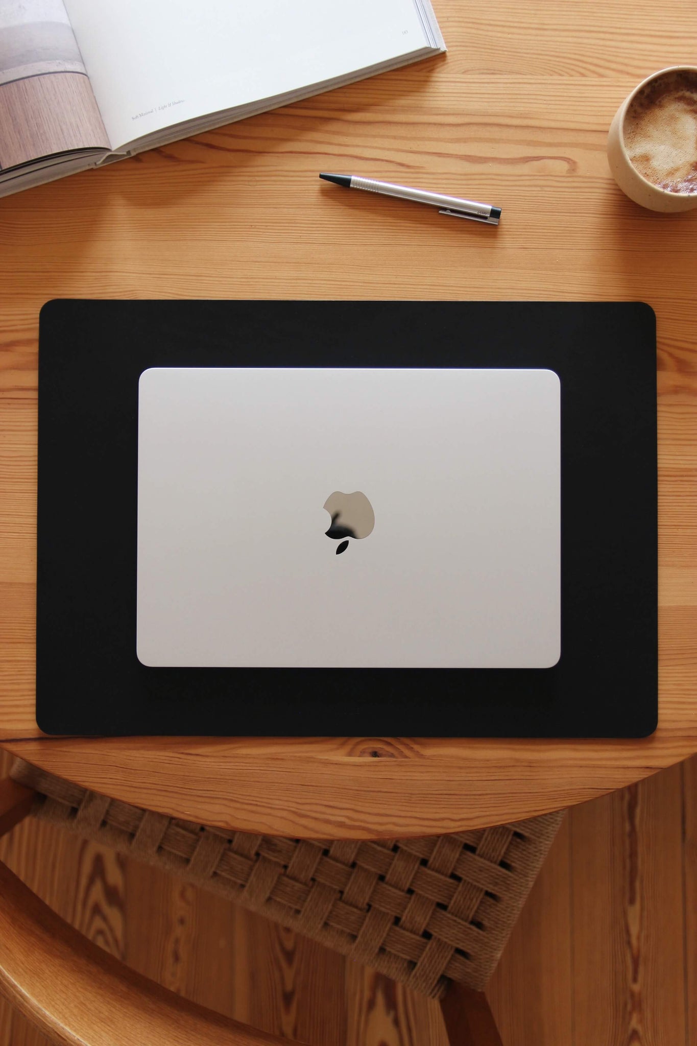 Auf einem Holztisch liegt einer Schreibtischunterlage aus Leder in Schwarz und auf dieser befindet sich ein zugeklapptes MacBook.