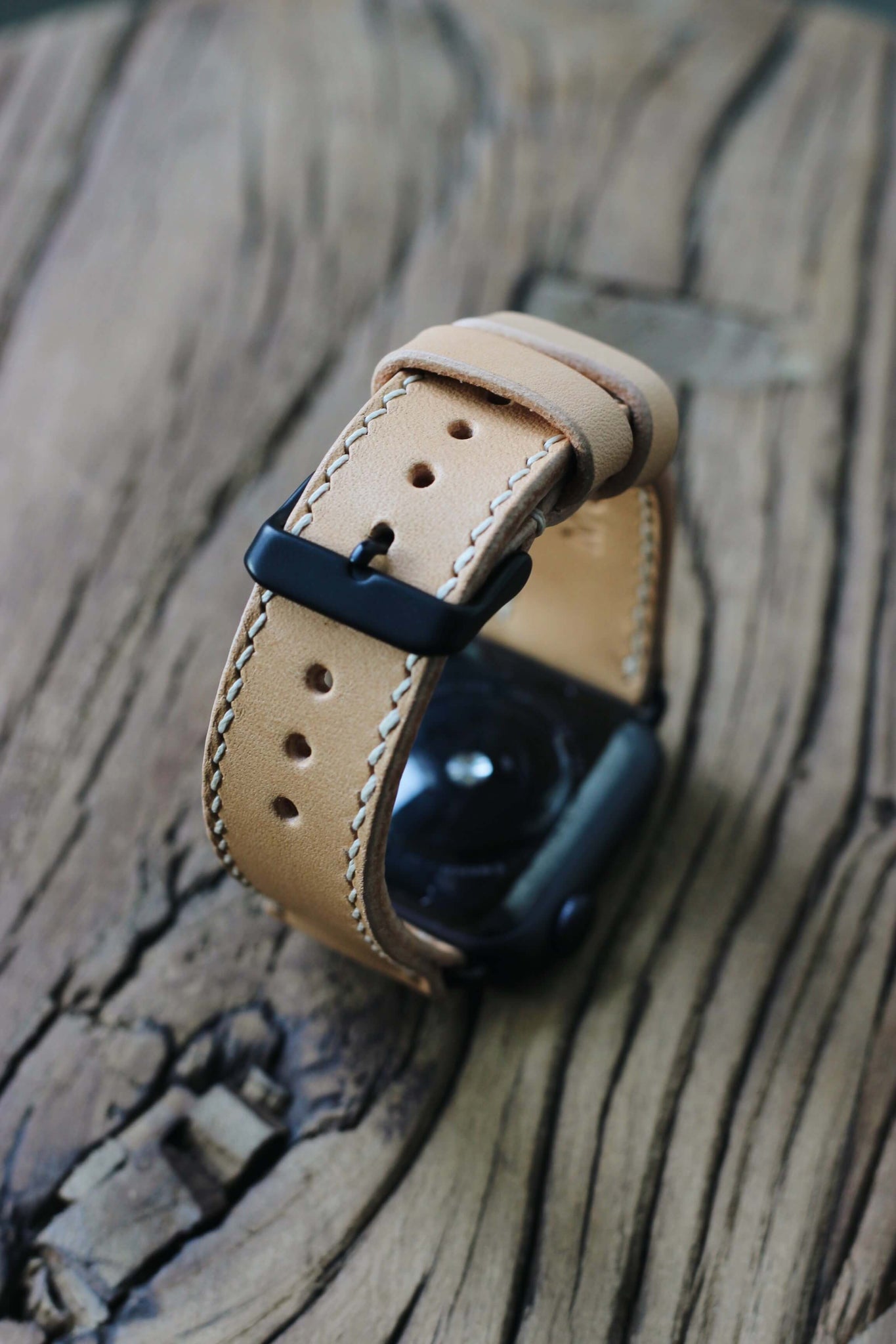 Apple Watch mit einem Apple Watch Lederarmband in Natural auf einer Holzplatte.