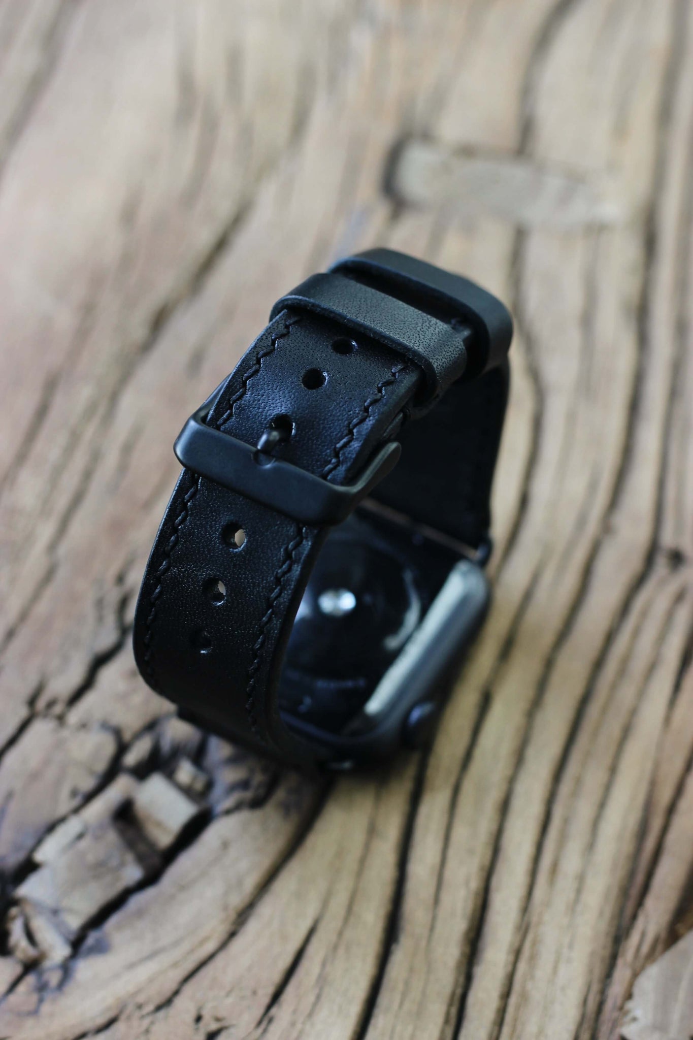 Apple Watch mit einem Apple Watch Lederarmband in Schwarz auf einer Holzplatte.
