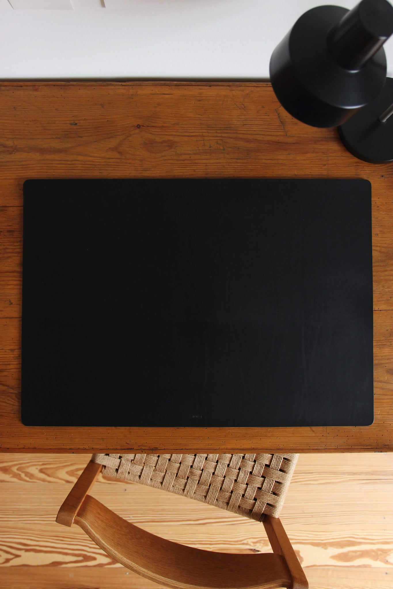 Eine große Leder Schreibtischunterlage in Schwarz liegt auf einem Schreibtisch aus Holz.